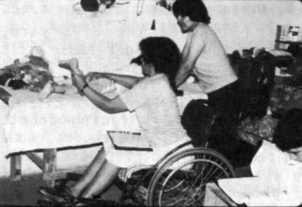 Mari (antes del brote de su infección ósea) examina a un niño discapacitado, mientras que Julio, un miembro del equipo cuadripléjico, se refiere al Manual 'El Niño Campesino Deshabilitado' que está a punto de completarse.