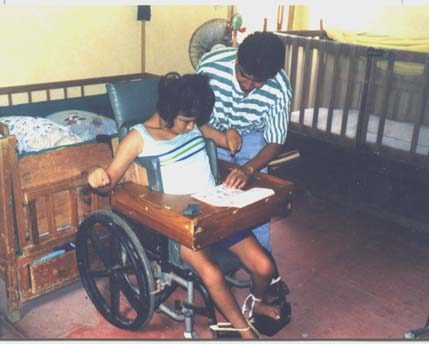 Un ayudante en Piña Palmera usa un juego de tableros para ayudar a una niña con parálisis cerebral a decir lo que quiere señalando los dibujos apropiados.