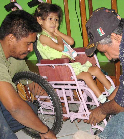 En la tienda de sillas de ruedas PROJIMO de Duranguito, con la ayuda de su padre, Raymundo hace los ajustes finales a una silla hecha a medida para esta niña. Consulte el inserto adjunto para obtener una actualización del Proyecto PROJIMO.