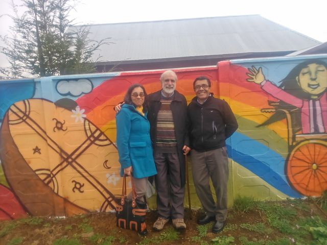 Eliana Mellado y Eduardo Herrera, director y codirectores de la Escuela de Terapia Ocupacional, posan conmigo frente al mural pintado por miembros de la Unión de Niños y Padres por la Integración Normal.