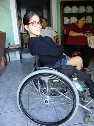 Mónica se sienta en su silla de ruedas sobre su cojín Roho, que estaba destinado a protegerla contra las escaras, pero no lo hizo. (Para problemas con su silla de ruedas, como el respaldo bajo, visto aquí, vea la sección "Otros problemas" más adelante en este boletín).