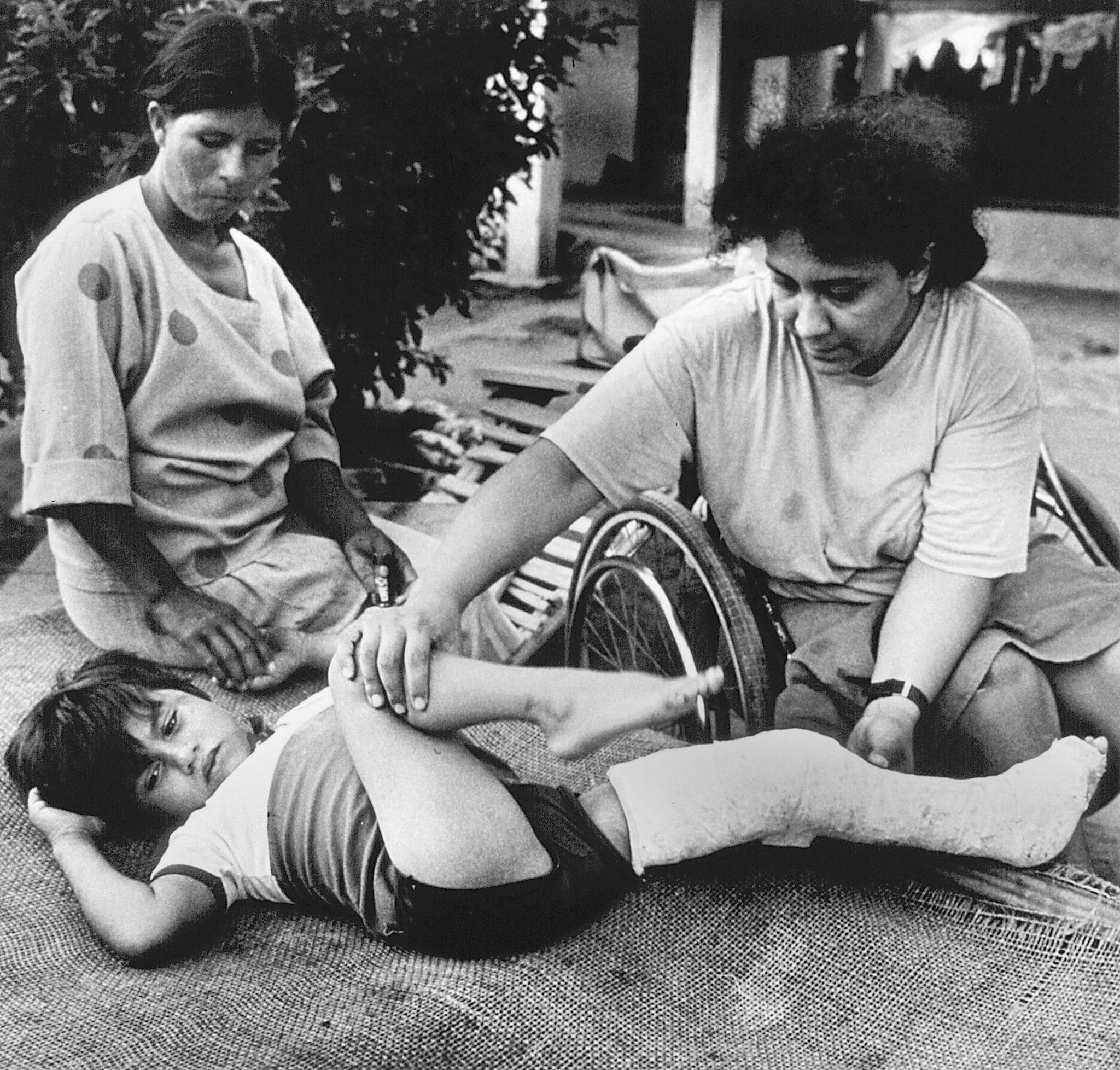 Rehabilitation coordinator Mari Picos (in wheelchair) teaches Manuelito's mother the physical therapy that will enable him to walk.