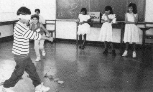 Learning about seeing and hearing. The blindfolded child tries to point to children as they sneak up to "steal' his rocks. Later the children test one another's sight and hearing.