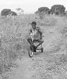 On his way home from school, Pafupi rides his improved "narrow gauge" tricycle, designed for the narrow trails.