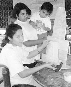 Marielos, who is paraplegic, makes a special standing frame for a child, who watches with interest from his mother’s arms. Marielos also makes doll-house furniture, for which she has more requests for sales than she can meet.