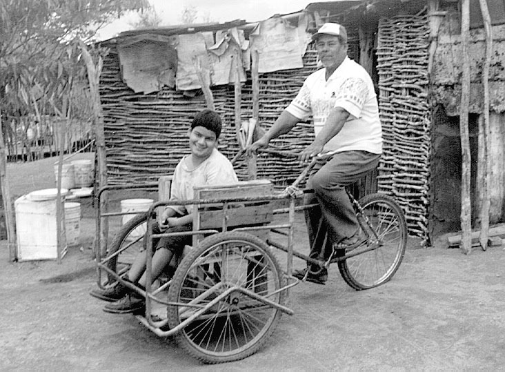 Daniel, with his daughter, Eli, in front of their home. Eli sits in the cargo tricycle he adapted to carry her.
