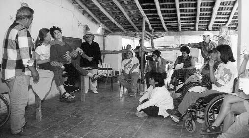 Working with course pariticipants at PROJIMO, Jean Anne holds Xochi between her legs to explore her range of motion, how to improve her position, and the type of adaptive seating, wedges, and supports that will help her sit as best she can.