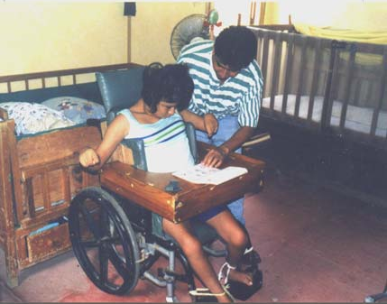 A helper at Piña Palmera uses a set of picture boards to help a girl with cerebral palsy say what she wants by pointing to the appropriate drawings.