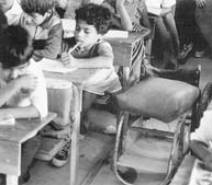 A disabled boy in the classroom, with his wheelchair beside him.
